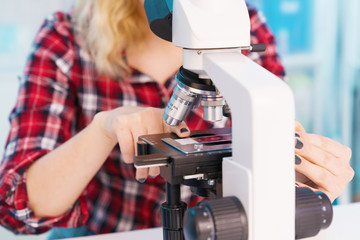 Young woman medical researcher looking through microscop on slide