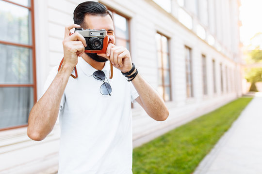 Stylish hipster with a beard and a camera, taking pictures, walking around the city