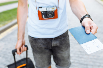 A man with a suitcase and a camera, holding a passport and tickets close-up