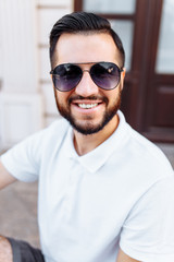 Stylish hipster in a white t-shirt and with a beard, standing near a white wooden wall