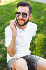 Business and stylish hipster in a white shirt, sitting on the lawn in the Park and talking on the phone