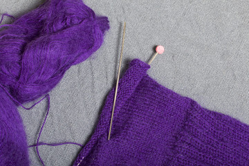 Knitting with steel knitting needles. A ball of purple thread and steel knitting needles in an unfinished knit.