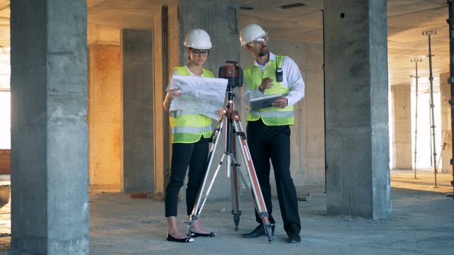 Construction site with two architects discussing something near land surveying equipment