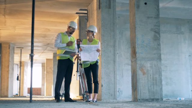 Construction site with two builders, constructors discuss a blueprint.