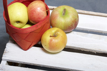 Ripe aromatic apples in a wicker basket. Located on a wooden box, knocked out of the boards.