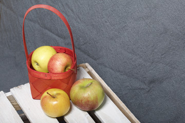 Ripe aromatic apples in a wicker basket. Located on a wooden box, knocked out of the boards.