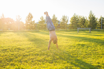 Yoga, fitness and healthy lifestyle concept - man doing a handstand on summer nature