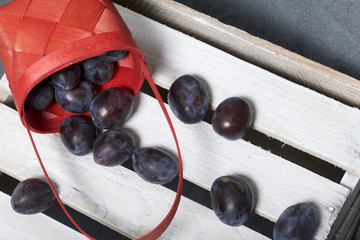 Ripe fragrant plums in a wicker basket. Located on a wooden box, knocked out of the boards.