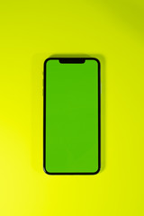 Green chroma key on smartphone as hero object on bright glamorous modern neon pop yellow background - smartphone telephone with OLED display