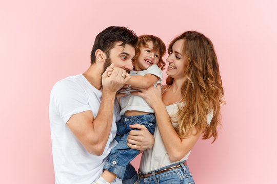 A Happy Family On Pink Studio Background. The Father, Mother And Son Posing Together