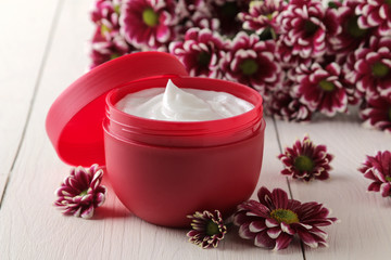 Fototapeta na wymiar Cream in a red jar close-up and flowers of chrysanthemum on a white wooden table. cosmetics