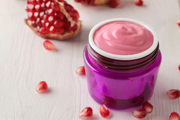 Cosmetic cream in a lilac jar and with fresh pomegranate on a white wooden table. pomegranate extract. cosmetics.