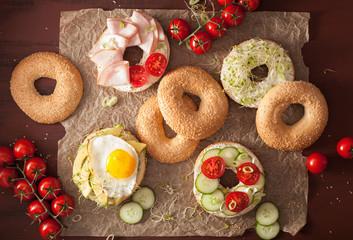 variety of sandwiches on bagels: egg, avocado, ham, tomato, soft cheese, alfalfa sprouts