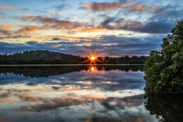 Obraz premium Sun rising against cloudy sky with reflection in river