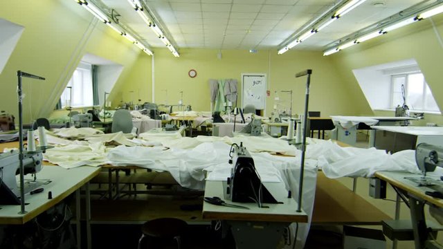 View over empty sewing factory with pieces of white fabric and sewing machines left on tables