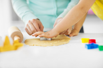 family, cooking and people concept - mother and little daughter with molds making cookies from dough at home kitchen
