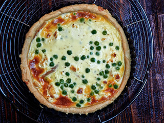 Smoked trout, goat cheese and peas quiche, set on a cooling rack, on a dark  brown wooden board