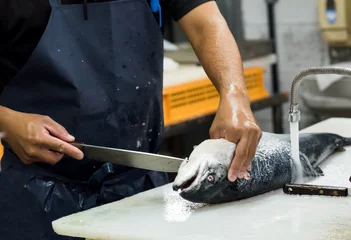 Crédence de cuisine en verre imprimé Poisson homme filetant le saumon sur une planche à découper blanche, le chef coupant du poisson à table