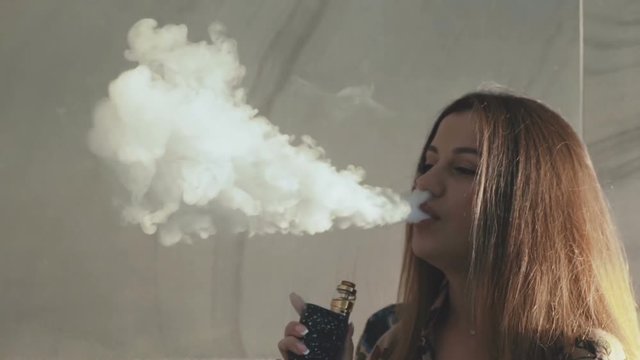 Macro shot of vaporing dense clouds of smoke of pretty girl