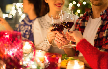 holidays and celebration concept - close up of happy friends having christmas dinner at home, drinking red wine and clinking glasses