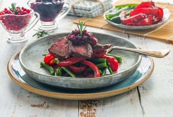 Sliced venison steak with lingonberry sauce, roast red peppers and green beans