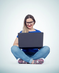 Naklejka premium Happy young woman with smile working or typing on laptop while sitting in lotus pose on the floor over light background