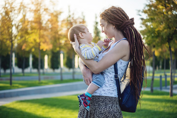 Young modern happy mom with baby son walking in Sunny Park. Concept of the joy of motherhood and...
