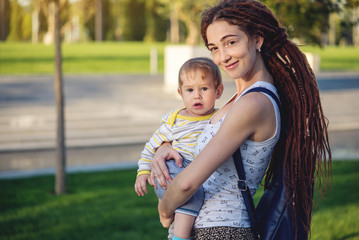 Fototapeta premium Young modern happy mom with baby son walking in Sunny Park. Joy of motherhood and autumn mood