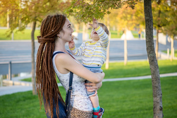 Young modern mom with baby son walking in Sunny Park. Concept of the joy of motherhood