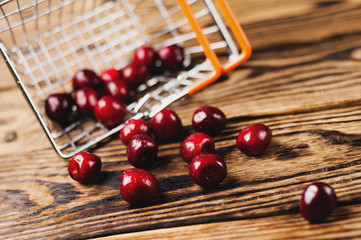 Fresh red cherries poured out of metal market basket on old brown wooden table. Business concept