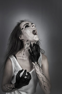Portrait screaming mad girl with black veins on her face clawing his neck. concept of halloween and day of the dead. halloween makeup