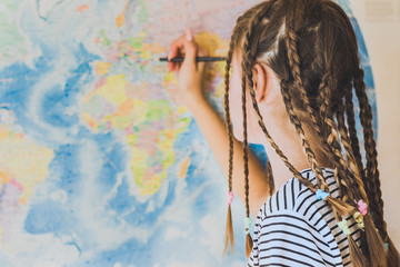 Teenage girl with pigtails makes pencil marks on the world map