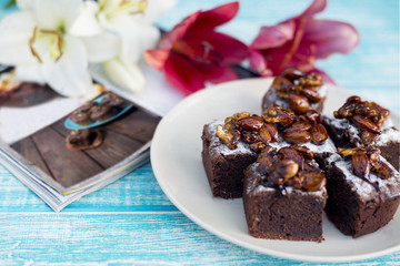 Pieces of chocolate cake with nuts on a plate next to the flowers of lilies.