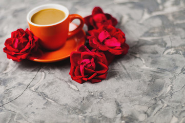 Full cup of coffee with milk beside red roses on old gray concrete surface. Love concept