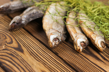 Heap of dried salted fishes under green wicker fishing net on rustic brown wooden table with copy space for your text