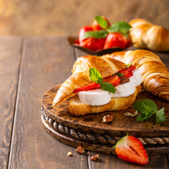 Fresh sandwich with croissant with goat cheese, strawberries, honey and pecans on wooden cutting board with copy space.