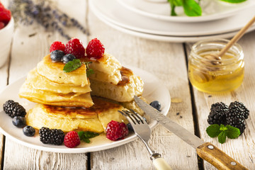 Pancakes with forest fruits berries on white table.