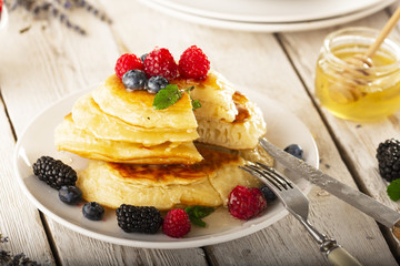 Pancakes with forest fruits berries on white table.