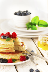 Pancakes with forest fruits berries on white table.
