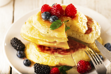 Pancakes with forest fruits berries on white table.
