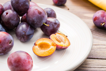 Many whole ripe berries of blue plum and one bisected berry on a plate on a wooden table