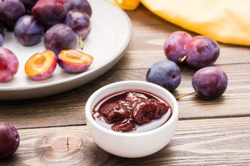 Appetizing jam from blue plum and a bunch of ripe berries on a plate on a wooden table