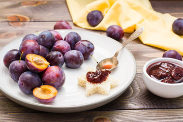 Bruschetta with plum jam and ripe blue plum berries on a plate on a wooden table