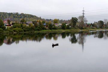village on the bank of the autumn river in cloudy weather, in the middle of the river you can see a boat with a fisherman