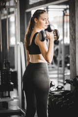 Fototapeta na wymiar Fit beautiful young woman caucasian posing at the camera in sportswear. Young woman holding dumbbell during an exercise class in a gym. Healthy sports lifestyle, Fitness concept. With copy space.