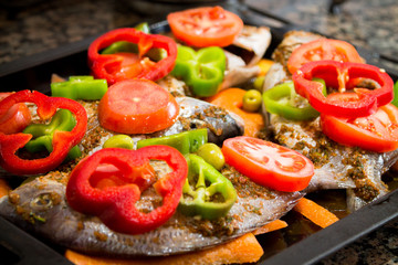 A black baking tray with raw dorado fish and sliced ​​fresh vegetables. Harvest for baking. Cooking cooking