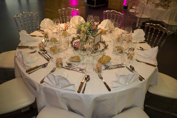 white chairs and round table for guests served with cutlery flowers and covered with a tablecloth
