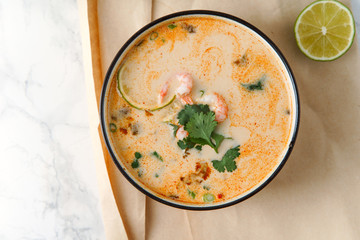 Tom yum soup with shrimps, traditional thai spicy dish served with cilantro and lime slices on marble table. Top view with copy space