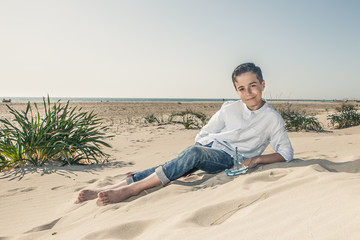 boy sitting on the beach sand in a white dress