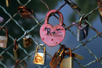 A heart shaped pink padlock attached to wire fence on a bridge. Locks bridge.
